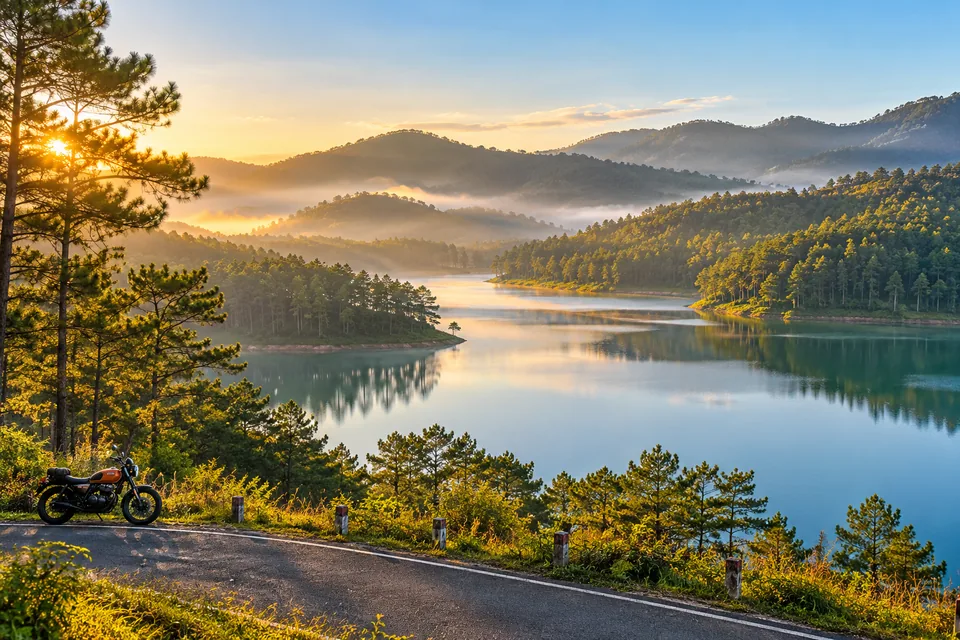 Pine-covered hills and a misty lake in Da Lat with a parked touring motorcycle