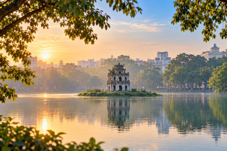 Turtle Tower on Hoan Kiem Lake in Hanoi framed by leafy trees at sunrise